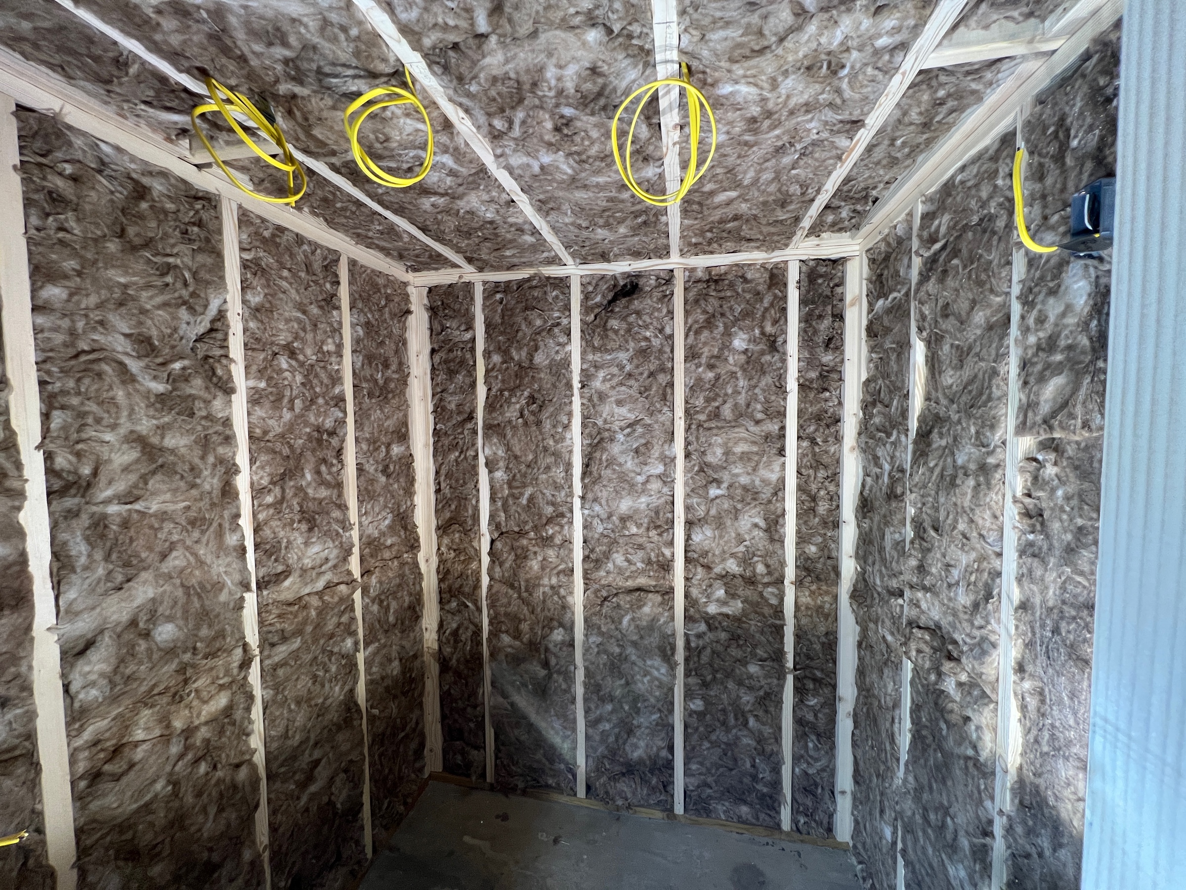 A small framed room with studs exposed and fiberglass insulation filling the voids between the studs