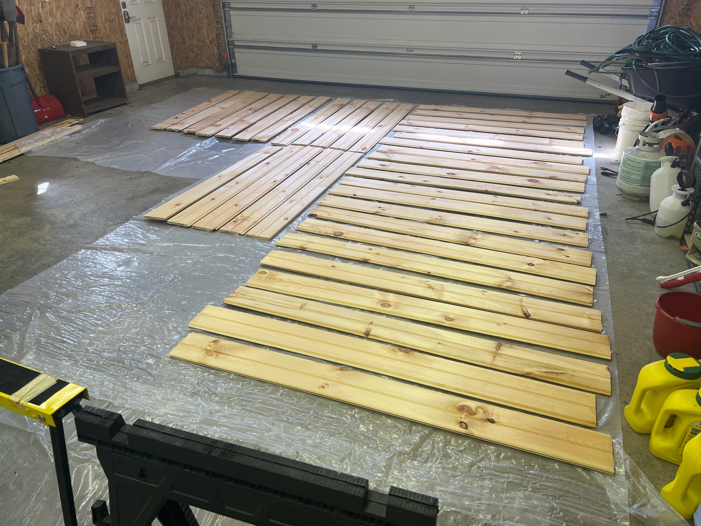 About 40 planks of tongue-and-groove knotty pine, laying on plastic sheets on a garage floor