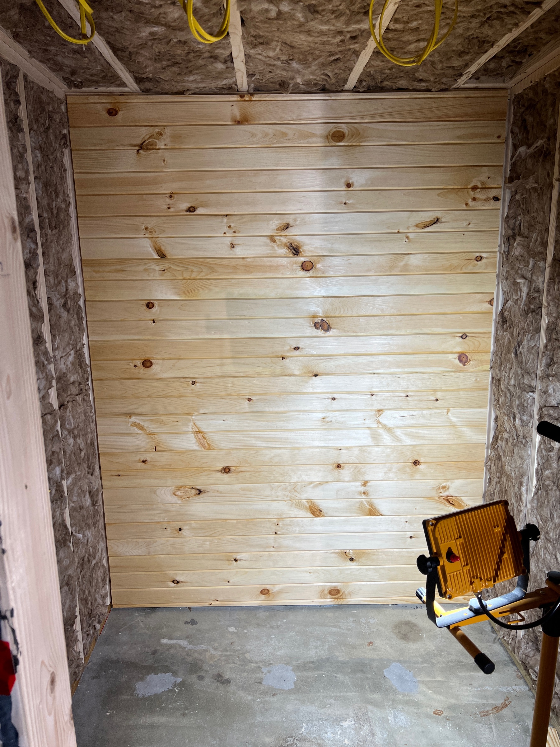 The back wall of a soon-to-be wine cellar sided with unstained knotty pine, hung so boards run horizontally.