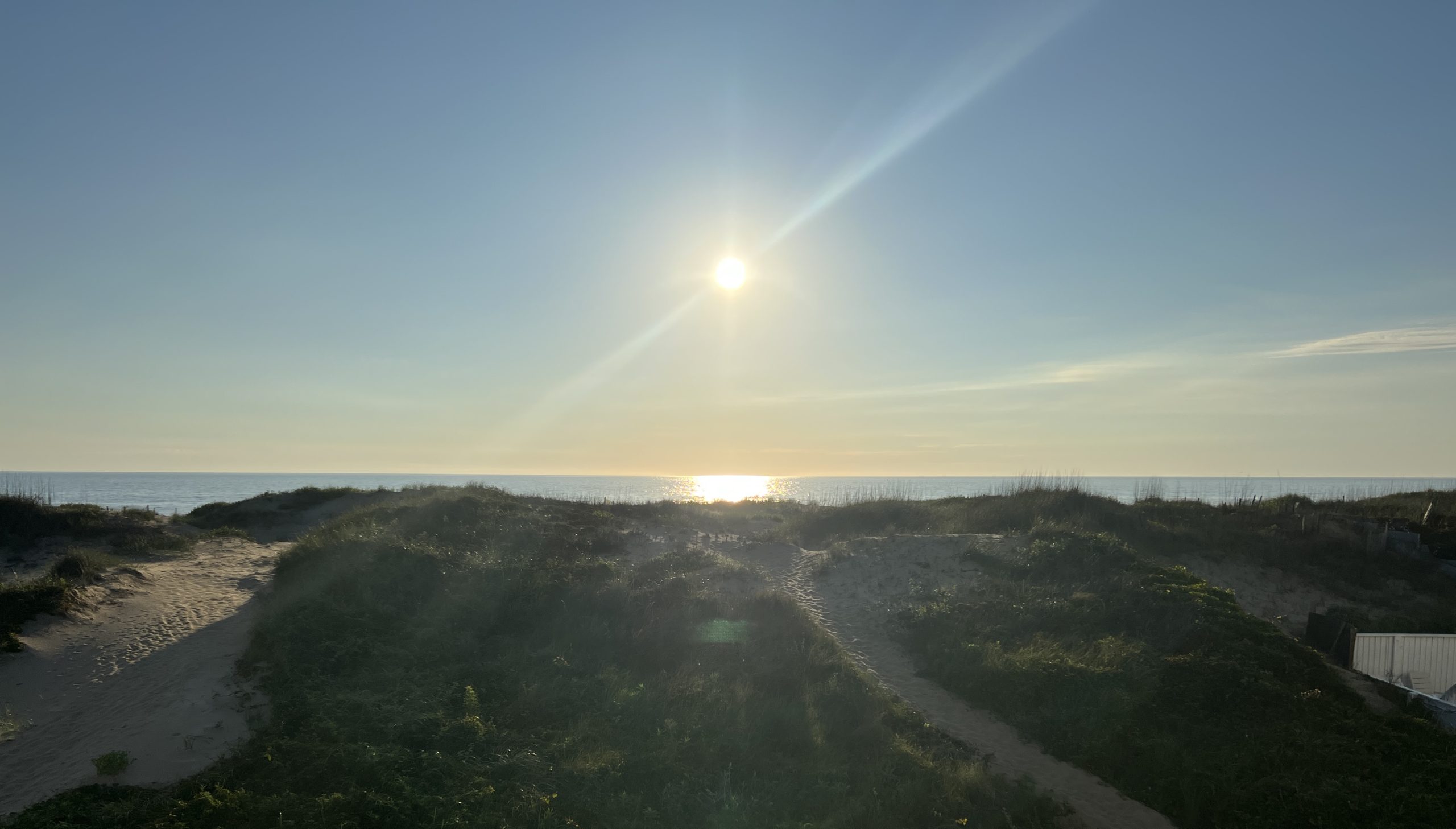 The Sun rising over the Atlantic Ocean, with a dune in the foreground.