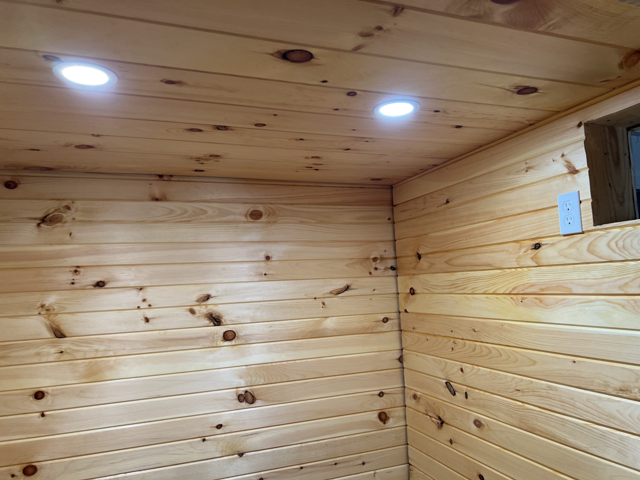 The finished ceiling showing installed can lights and an electrical outlet on the side wall.